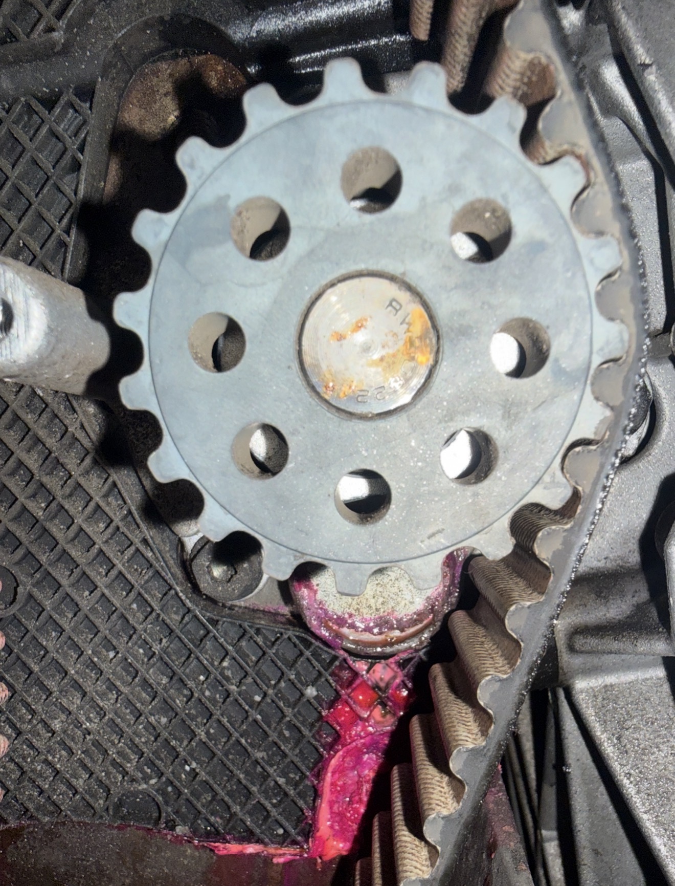 Water-pump area beside a toothed belt, with pink residue below the pulley and on the housing